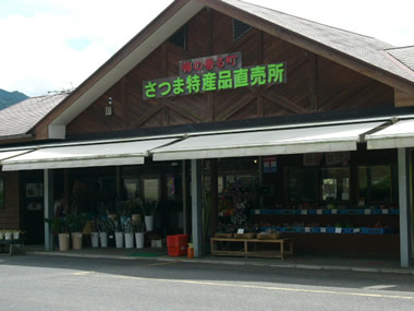 花などの商品が店頭に並べられているさつま特産品直売所の外観写真