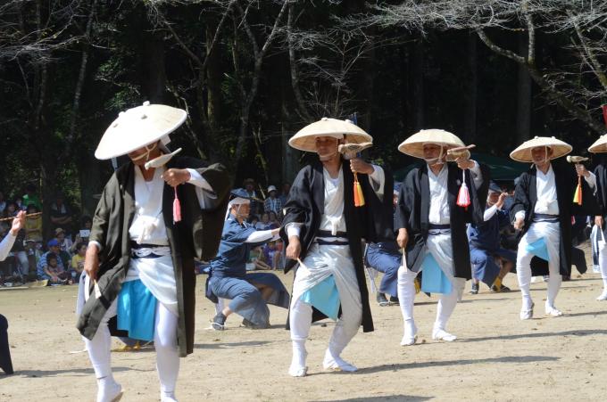 傘を被り小鳥の模型を持って踊る男性たちの写真