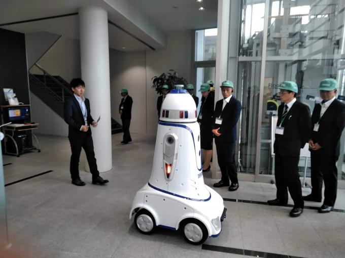 構内を動く自動監視ロボットを見ながら説明を聞く参加者たちの写真