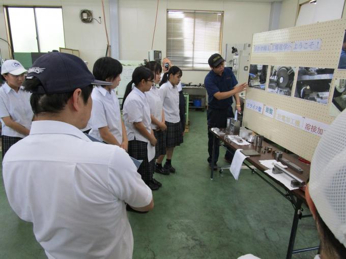ホワイトボードに写真を貼って説明する作業員と、話を聞く生徒達の写真