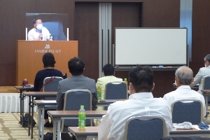演壇で話をする議員と、座って話を聞いている議員たちの写真