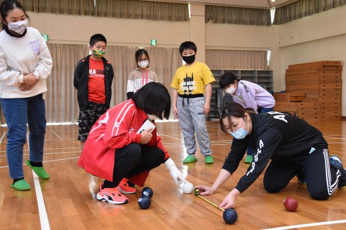 体育館で投げたボールの距離を女性が測っている写真