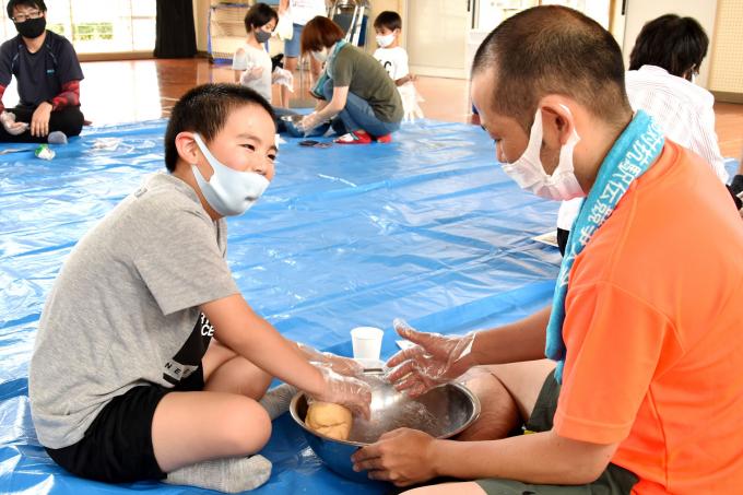 ボールでパン生地をこねる男の子と、説明する男性の写真