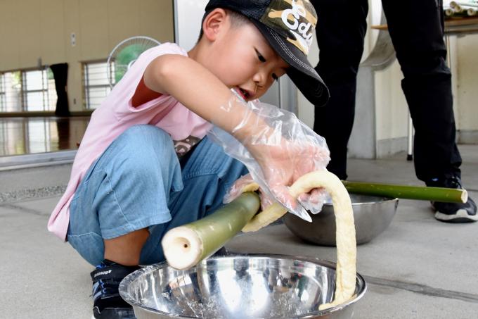 竹に生地を巻き付けている男の子の写真