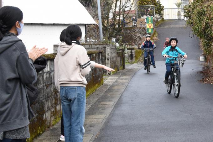 自転車に乗って走る小学生を沿道から応援する保護者の写真