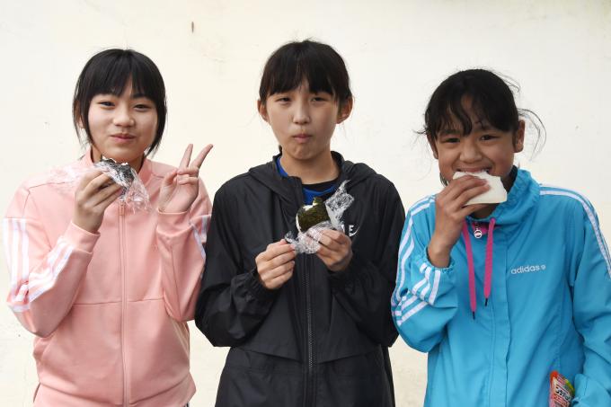 並んでおにぎりやサンドイッチを食べる小学生の写真