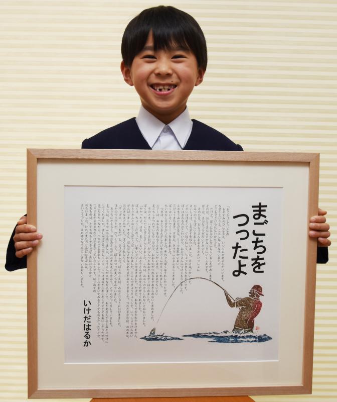 額に入った作文の文面を見せて記念撮影する池田君の写真