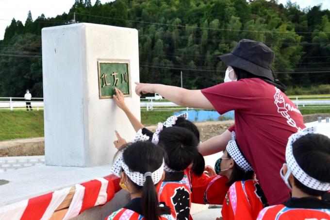 北方川と書かれたプレートを子供達が指差している写真