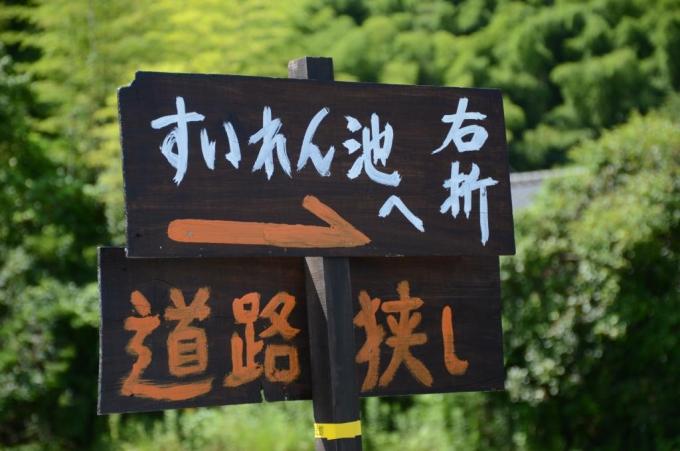 「すいれん池へ 右折 道路狭し」と書かれた案内看板の写真