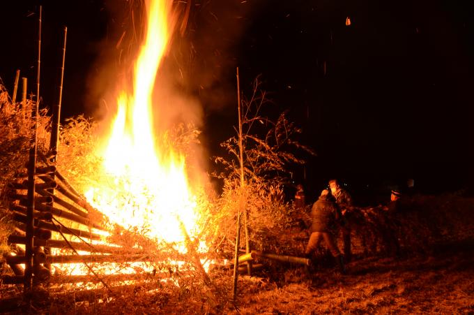 焚き火の側で、焚き火にくべる正月飾りを運ぶ人たちの写真