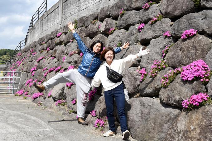 芝桜の植栽された岩をバックにポーズをとる男性と女性の写真