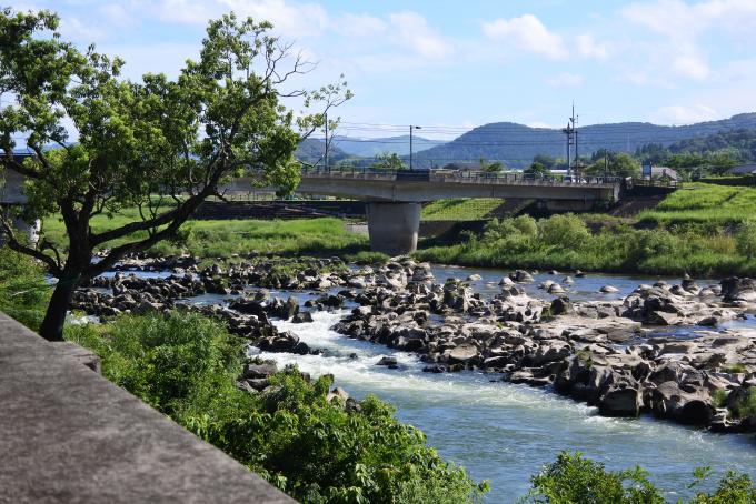 岩がゴロゴロしている間を流れる川の奥に橋が映る写真
