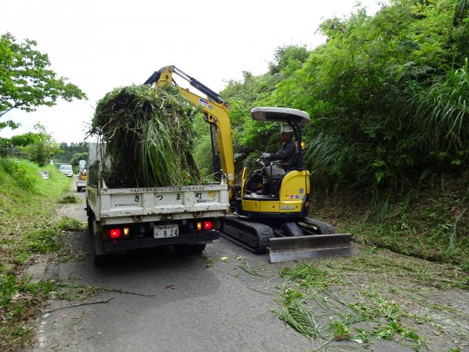 ショベルカーで道路敷地の除草作業をおこなっている様子の写真