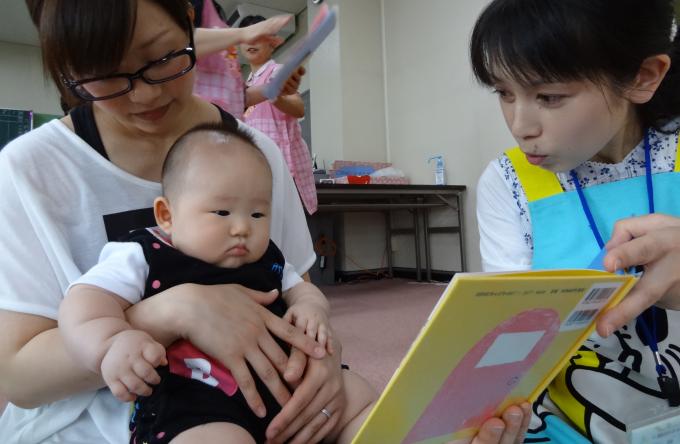 女性が赤ちゃんに絵本を見せている写真