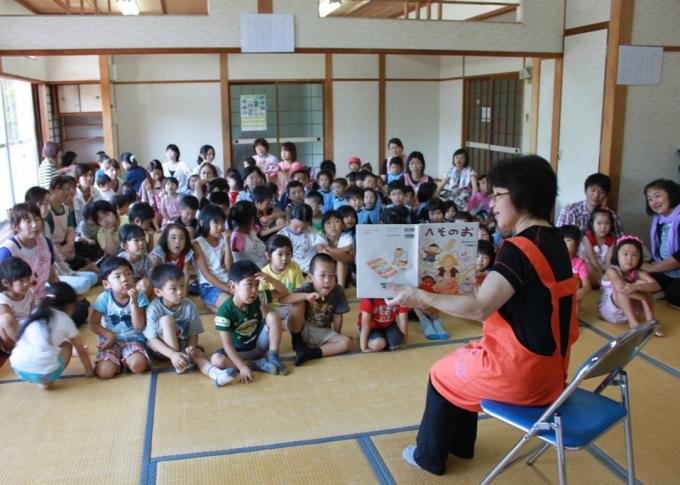 広間で女性が子どもたちに読み聞かせしている写真