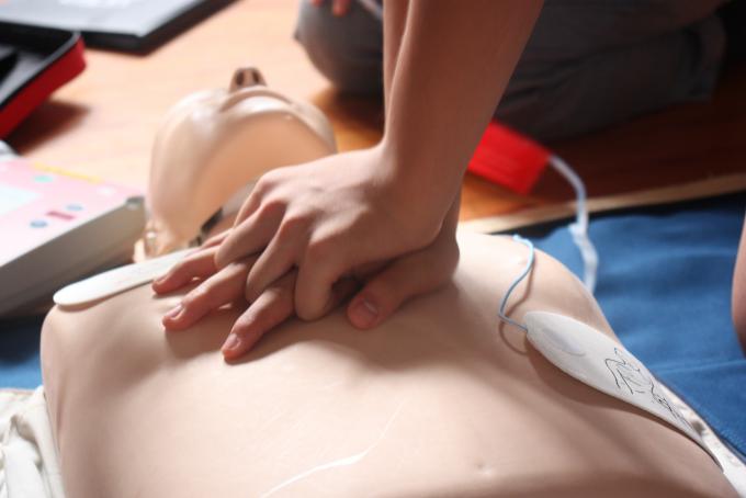 AEDをつけたダミー人形を心臓マッサージしている手元を写した写真